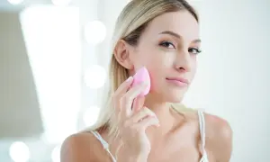 Kobieta z blond włosami delikatnie nakłada podkład gąbeczką, tworząc lekki makijaż.