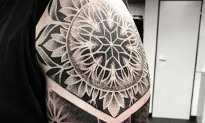 Imponujący, czarno-biały **mandala tatuaż** na ramieniu, z geometrycznymi wzorami i detalami wykonanymi techniką dotwork.