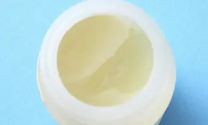Wazelina, czyli paraffinum liquidum, w białym słoiczku na niebieskim tle.