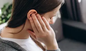 Kobieta dotyka ucha, czując dyskomfort. Może to być objaw problemów ze słuchem lub zapalenia, a nawet **wągrów w uchu**.