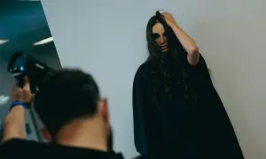 Modelka z mocnym makijażem pozuje do zdjęcia, fotograf trzyma aparat.