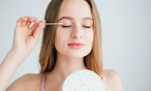 Młoda kobieta aplikuje wacikiem coś na powiekę. Zastanawia się, castor oil co to jest i jak może pomóc jej pielęgnacji.
