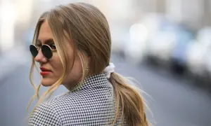 Kobieta w okularach przeciwsłonecznych i marynarce w kratkę, z blond kucykiem.