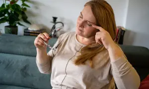 Kobieta z okładami na oczy, masuje skroń, trzymając okulary.