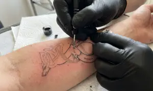 Artysta tworzy tatuaż wilka metodą handpoke na przedramieniu.