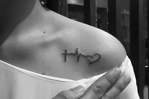 Tatuaż linia życia na ramieniu: krzyż, EKG i serce. Symbol wiary, życia i miłości.