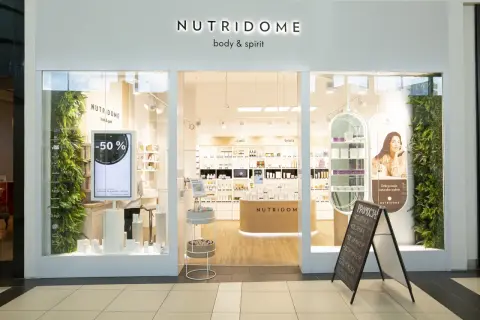 Sklep Nutridome z kosmetykami. W witrynie ekran z promocją -50%. W środku półki z produktami, a na zewnątrz tablica z ofertą specjalną.