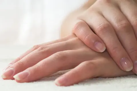 Delikatne dłonie z naturalnym, błyszczącym manicurem biologicznym. Paznokcie zadbane, z subtelnym połyskiem.