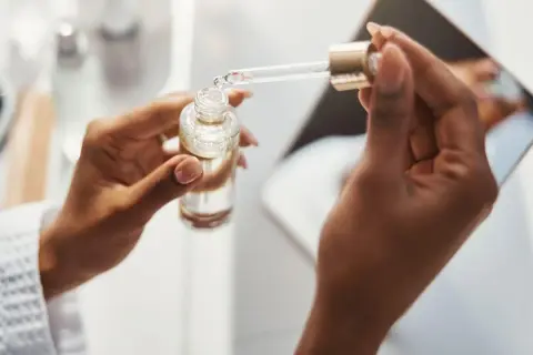 Dłonie trzymają buteleczkę z serum. Pipeta z kroplą produktu, być może zawierającego kwas ferulowy, jest gotowa do aplikacji.