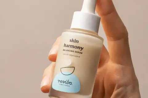 Dłoń trzyma buteleczkę serum Resibo Skin Harmony. Składnik alantoina wspiera regenerację skóry.