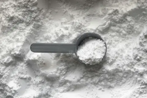 Miarka z białym proszkiem, prawdopodobnie disodium edta, na tle sypkiego materiału.