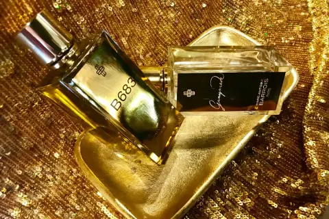 Dwa flakony perfum Marc Antoine Barrois na złotej, cekinowej tkaninie. Jeden flakon z napisem B683, drugi z nazwą "Ganymede".