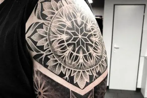 Imponujący, czarno-biały **mandala tatuaż** na ramieniu, z geometrycznymi wzorami i detalami wykonanymi techniką dotwork.