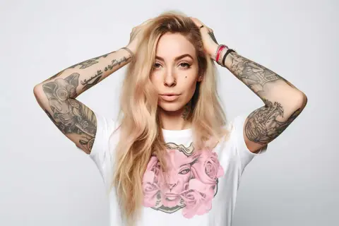 Kobieta z blond włosami i tatuażami na ramionach, prezentująca najnowsze tatuaże damskie. Na koszulce motyw róż.