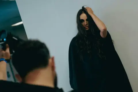 Modelka z mocnym makijażem pozuje do zdjęcia, fotograf trzyma aparat.