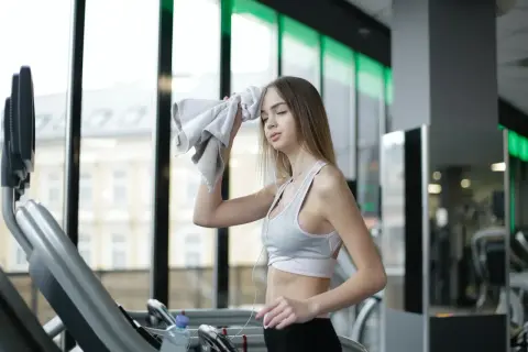 Zmęczona sportsmenka wyciera pot z czoła ręcznikiem. Intensywny trening to częste czego objawem jest pocenie się głowy.