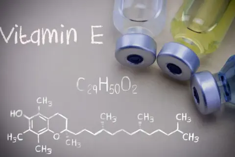 Wzór chemiczny witaminy E i fiolki z płynem. Witamina E jest ważna dla zdrowia.