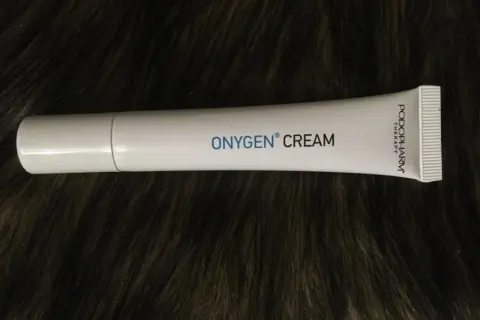 Biała tubka kremu OXYGEN CREAM na ciemnym, futrzanym tle.