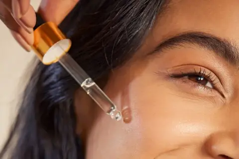 Kropla serum z pipetki zbliża się do skóry, ukazując subtelne retinol działanie.