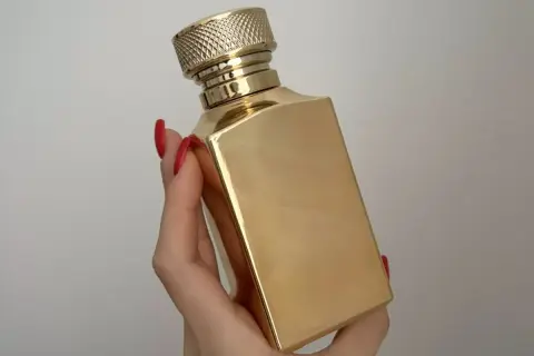 Złota butelka luksusowych perfum w dłoni z czerwonymi paznokciami. Elegancki flakon, który kusi zapachem.