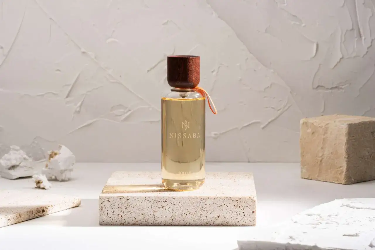 Elegancka butelka perfum NISSABA od Marc Antoine Barrois, z drewnianym korkiem, na kamiennym postumencie, w otoczeniu teksturalnych dekoracji.