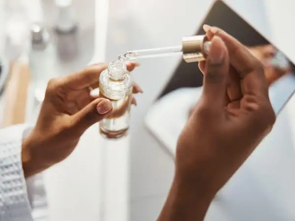 Dłonie trzymają buteleczkę z serum. Pipeta z kroplą produktu, być może zawierającego kwas ferulowy, jest gotowa do aplikacji.