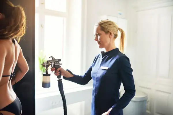 Opalanie natryskowe: wady mogą obejmować nierównomierne krycie i pomarańczowy odcień. Stylistka z pistoletem do opalania.