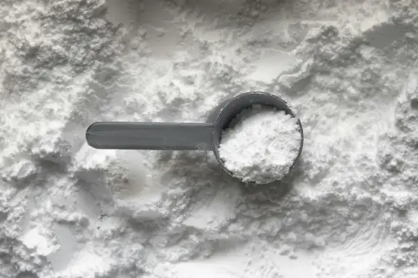 Miarka z białym proszkiem, prawdopodobnie disodium edta, na tle sypkiego materiału.