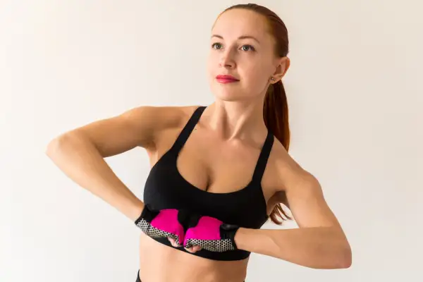 Kobieta w sportowym topie i rękawiczkach ćwiczy, pokazując jak ujędrnić piersi.