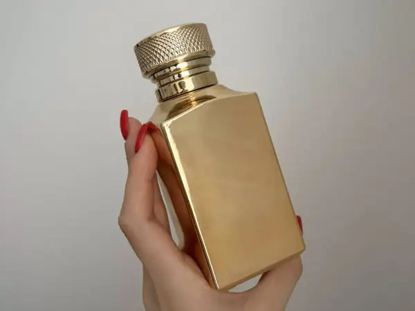 Złota butelka luksusowych perfum w dłoni z czerwonymi paznokciami. Elegancki flakon, który kusi zapachem.