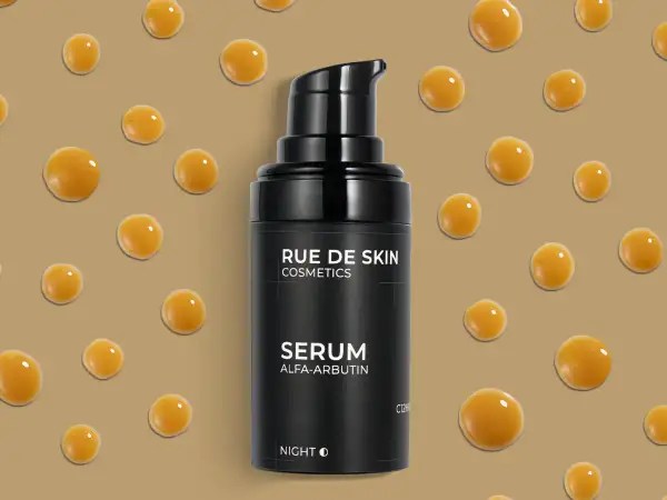 Czarny flakonik serum z alfa-arbutyną, otoczony kropelkami o bursztynowym kolorze.