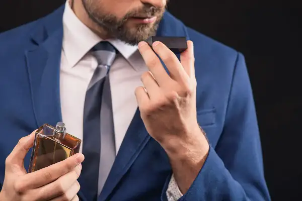 Elegancki mężczyzna w garniturze wącha perfumy. Czy to woda toaletowa czy perfumowana?